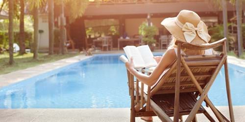 Woman reads a book by the pool of her hotel on holiday